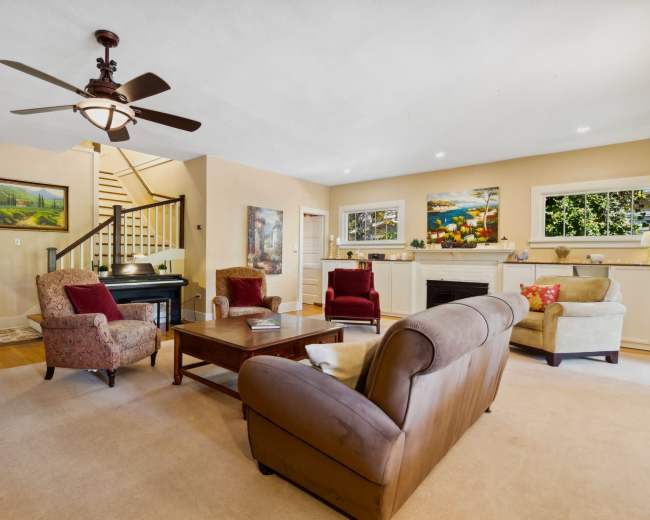 The living room features a cozy seating arrangement with two armchairs and a sofa, a coffee table in the center, and a staircase in the background leading to the upper floor.