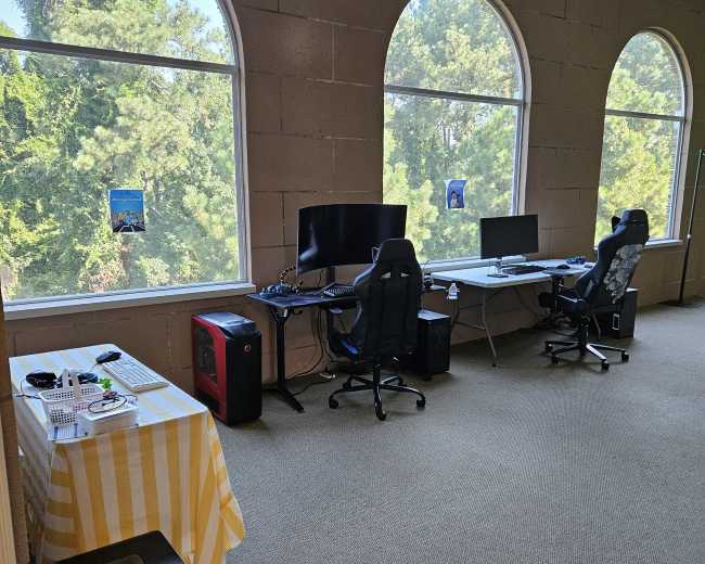 The image shows a spacious office with large arched windows, two desks with computers, and a yellow-striped tablecloth on a table holding a small printer.