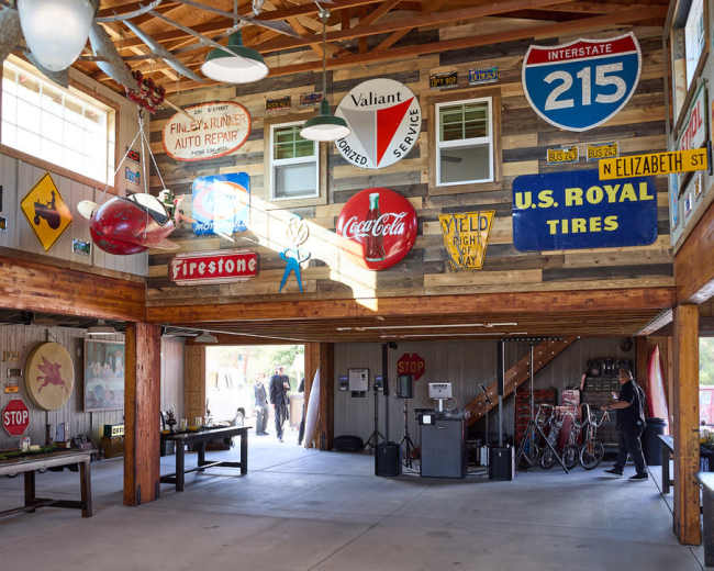 The image shows a vintage garage interior adorned with various advertising signs and memorabilia, with an open door leading outside.