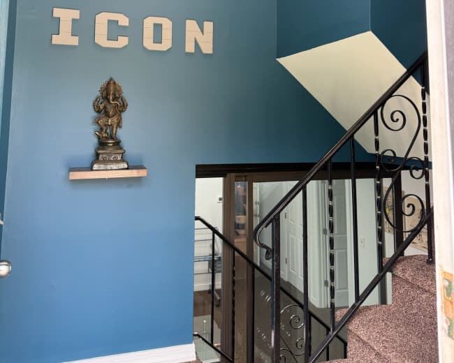 The image shows a brightly colored wall with the word "ICON" displayed, a decorative statue on a shelf, and a staircase leading to another level, accompanied by a modern light fixture.