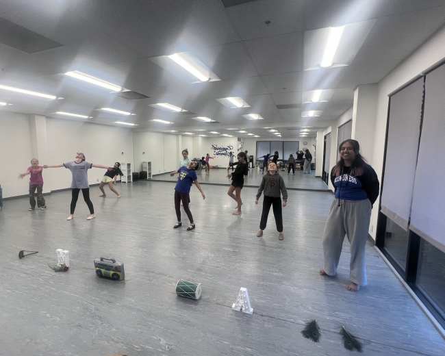 A group of children and teenagers are practicing a dance routine in a studio with mirrors and wooden flooring.