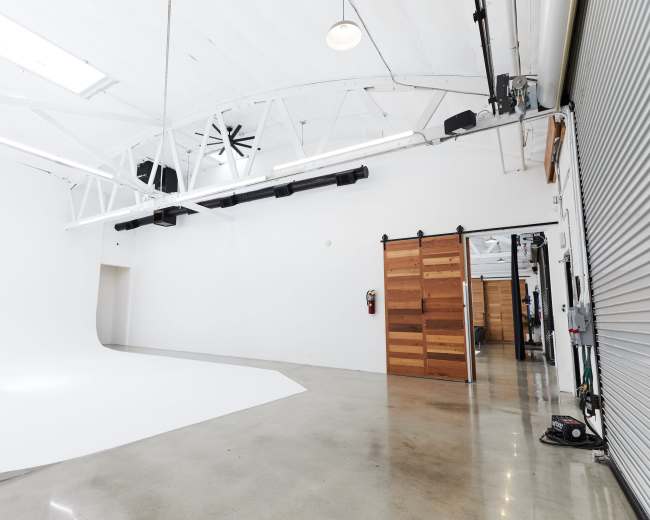 The image shows a spacious white studio with a seamless backdrop and large windows, featuring polished concrete floors and wooden sliding doors.