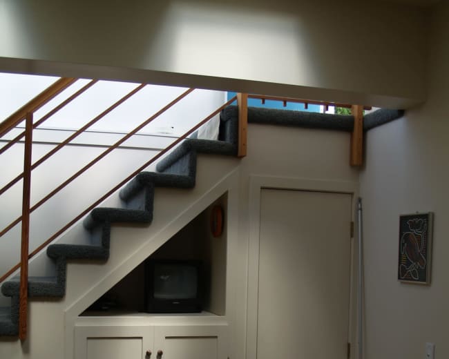The image shows a staircase leading to an upper level, with a small cupboard and a door beneath the steps and a television placed on top.