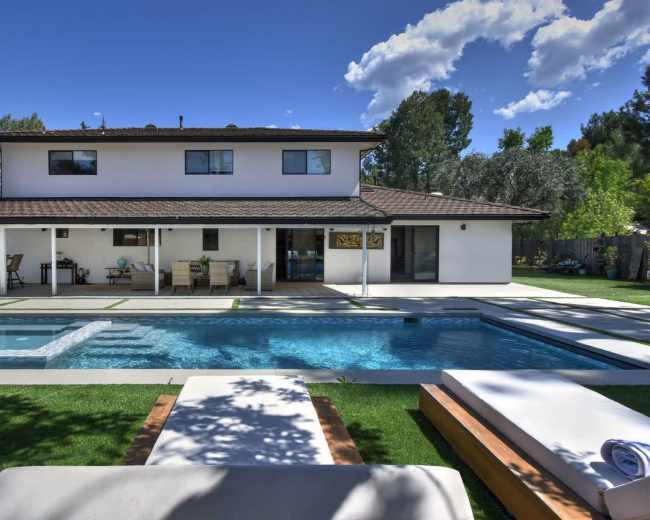 The image shows a two-story house with a landscaped backyard featuring a swimming pool, spa, and patio seating area.