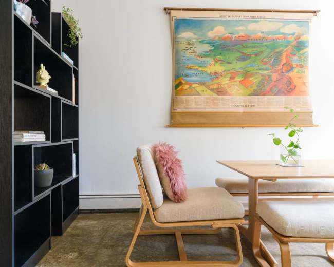 A dining area features a wooden table and chairs, with a large vintage map hanging on the wall behind them and a black bookshelf to the left.