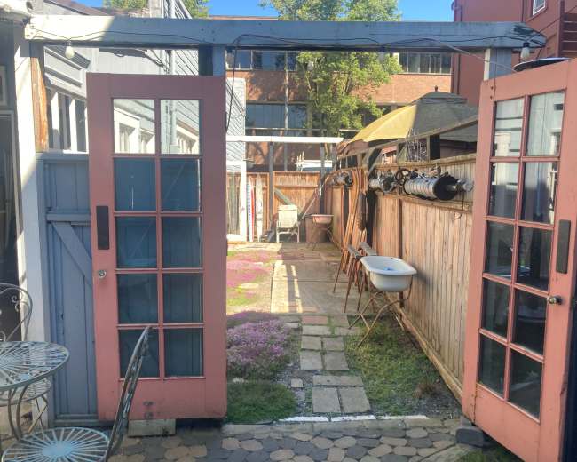 A view through pink double doors opening to a small, landscaped outdoor garden with a stone path and a few chairs.