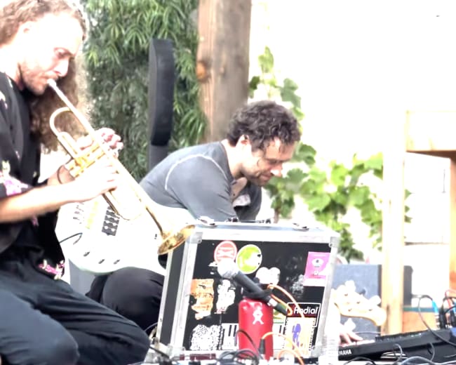 Two musicians perform on stage, one playing a trumpet and the other manipulating electronic equipment.