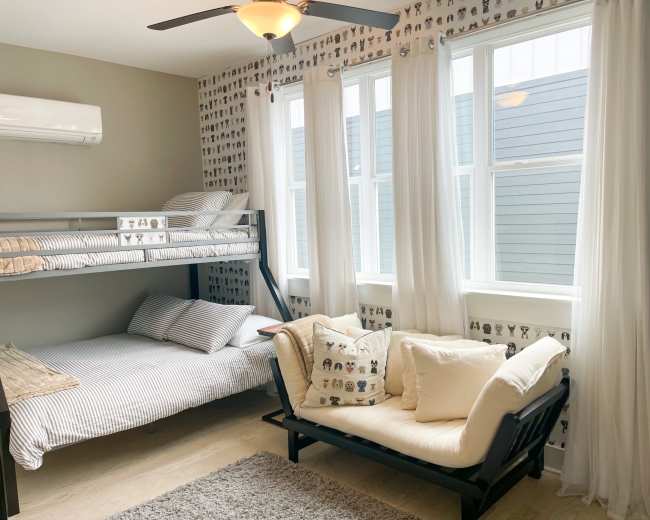 The room features a bunk bed on one side and a seating area with a daybed on the other, with large windows illuminating the space.