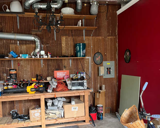 The image shows a cluttered garage with a workbench, tools, and various items, alongside a bicycle with a woven basket.