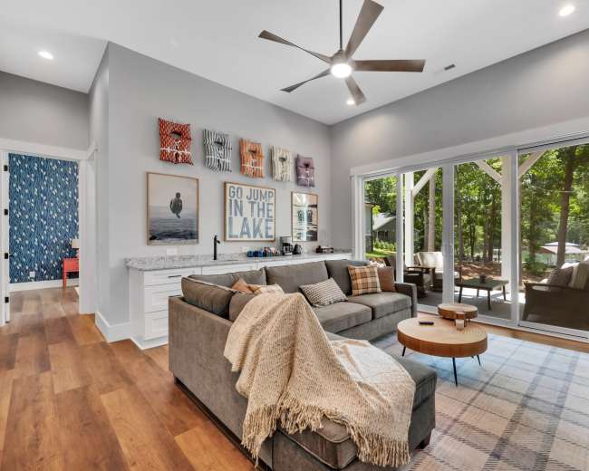 A modern living room features a sectional sofa, a coffee table, and large windows that overlook a wooded outdoor space.
