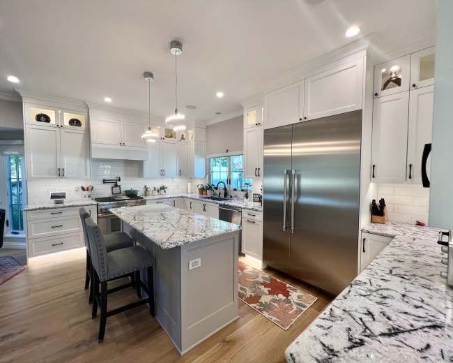 The image shows a modern kitchen featuring white cabinetry, a large island with seating, and stainless steel appliances, including a double door refrigerator.