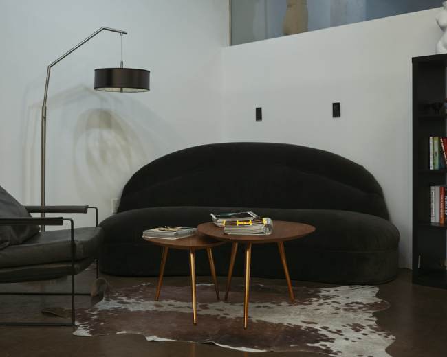 The image shows a modern living room setup featuring a curved black sofa, a sleek armchair, two wooden side tables, and a floor lamp.