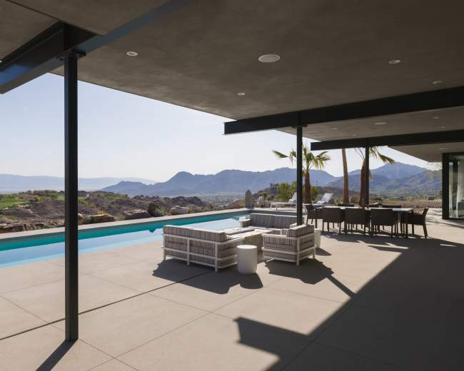 A modern patio features a swimming pool and a dining area, overlooking a mountainous landscape.