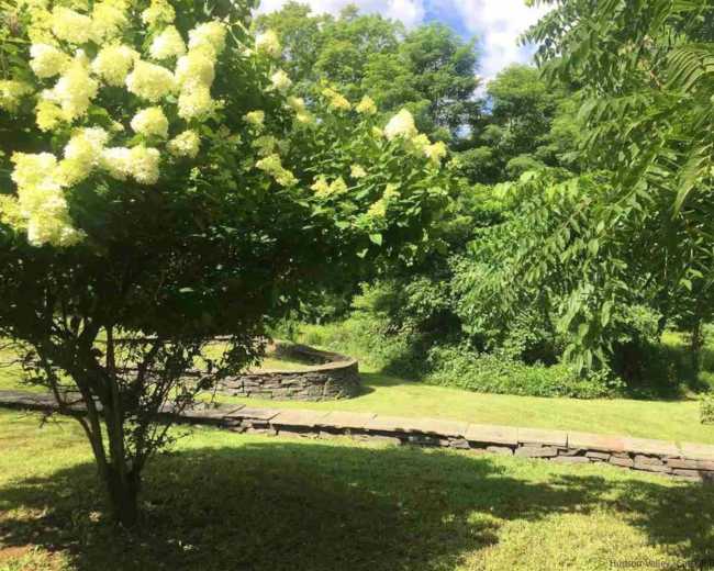A landscaped area features a path winding through greenery and flowering bushes under a blue sky.