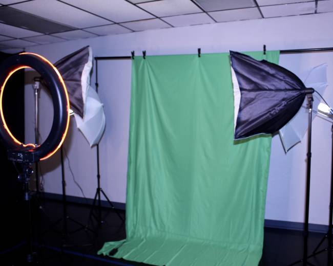 A photography setup featuring a green backdrop and multiple lighting devices, including a ring light and softboxes.