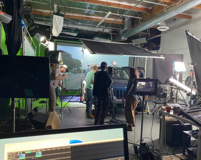 A film crew is shooting a scene involving a vehicle against a green screen in a studio.
