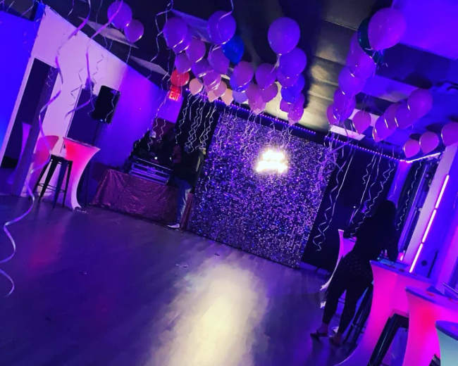 A decorated event space features colorful balloons, a sparkling backdrop, and illuminated tables.