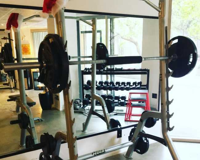 A weightlifting machine with a barbell and plates is set up in a gym, adorned with Santa hats.
