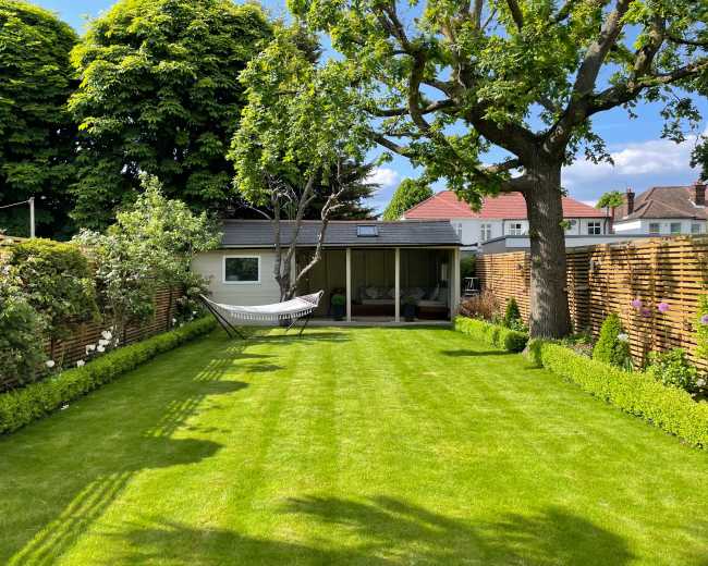 The image shows a well-maintained garden featuring a hammock, neatly trimmed grass, and wooden fencing on either side.