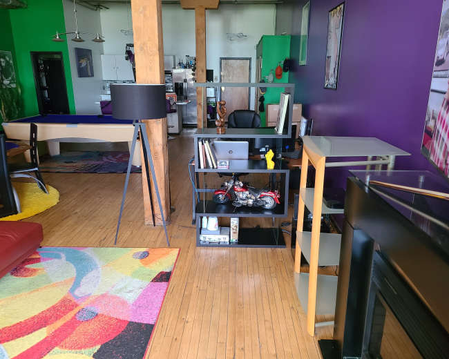A modern room with wooden floors featuring various furniture, including a desk, shelves with decorative items, and a colorful area rug.