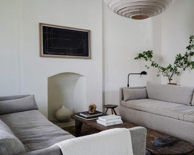 A minimalist living room features two light gray sofas, a wooden coffee table, and a wall adorned with a framed abstract artwork.