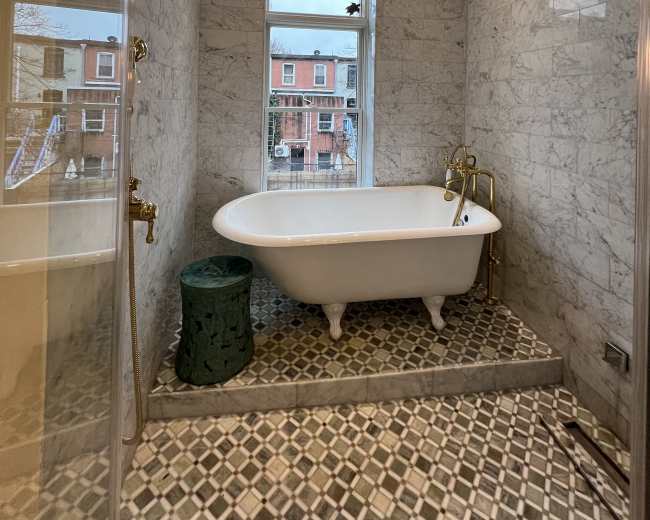 The image shows a modern bathroom featuring a freestanding bathtub, marble walls, and a tiled floor with a patterned design.