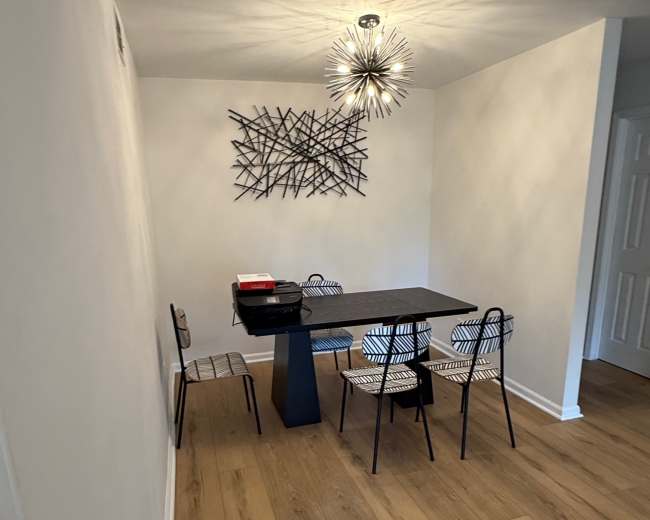 A dining area features a rectangular table with four striped chairs, a modern light fixture, and a wall art piece.