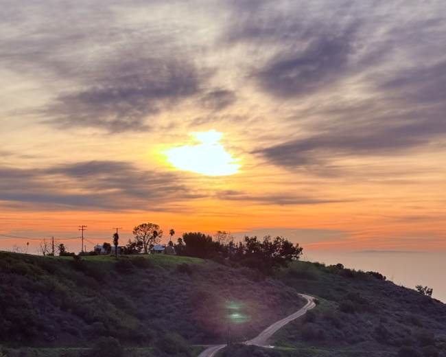 A winding dirt road leads along a hillside under a colorful sunset sky.