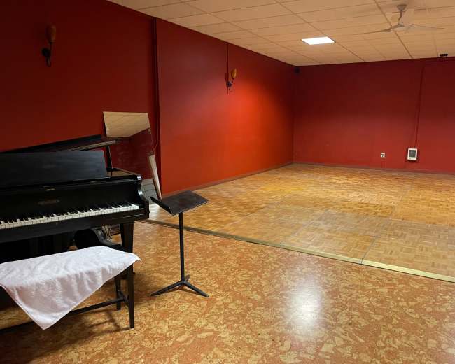 A room with red walls featuring a black piano, a music stand, and a wooden dance floor area.