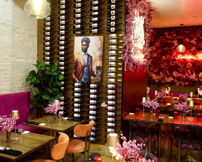 The image shows a stylish restaurant interior with a wine rack on the wall, floral decor, and tables set for dining.
