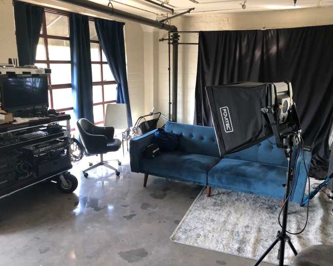 The image shows a photography studio with a blue couch, a light setup, and a backdrop on one side, alongside various pieces of equipment.