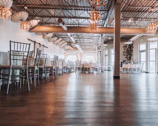 The image shows a spacious restaurant interior with wooden floors, elegant lighting fixtures, and neatly arranged table settings.