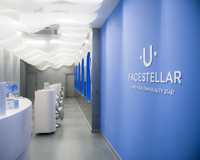 A modern beauty salon interior with a curved reception desk, sleek seating stations, and a wavy ceiling design.