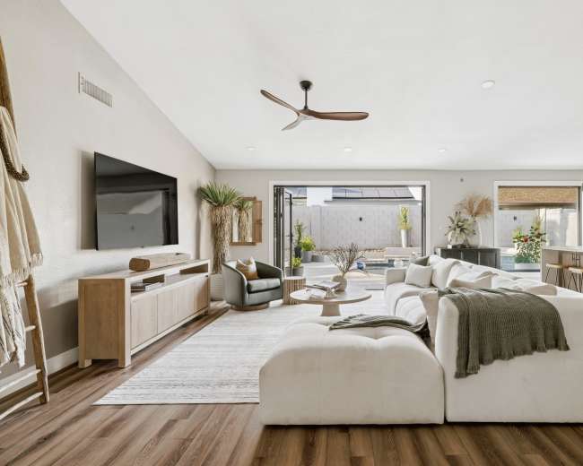The image shows a modern living room with a large sectional sofa, a TV mounted on the wall, and sliding glass doors leading to an outdoor area.