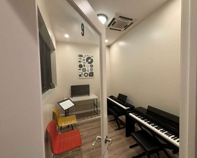 A small music room features a digital piano, a computer desk, and colorful seating, accessible through an open door.