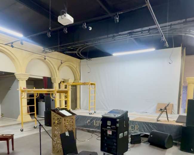 The image shows an empty performance space with equipment like speakers, a microphone stand, and staging materials scattered around.