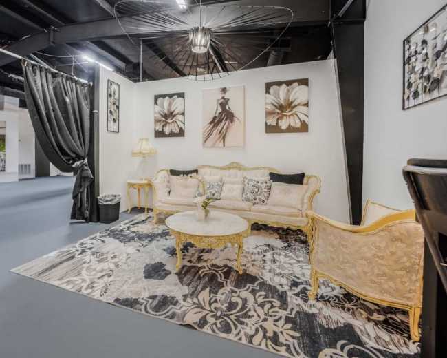 The image shows a elegantly decorated lounge area featuring a floral area rug, a vintage-style sofa, a round coffee table, and wall art on a white backdrop.