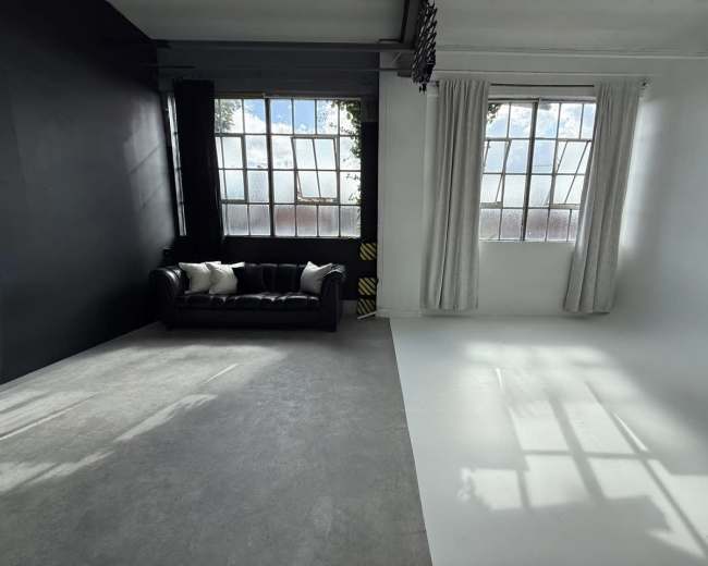The image shows a modern studio with a black wall on one side, a leather couch with pillows, and large windows allowing natural light to enter.