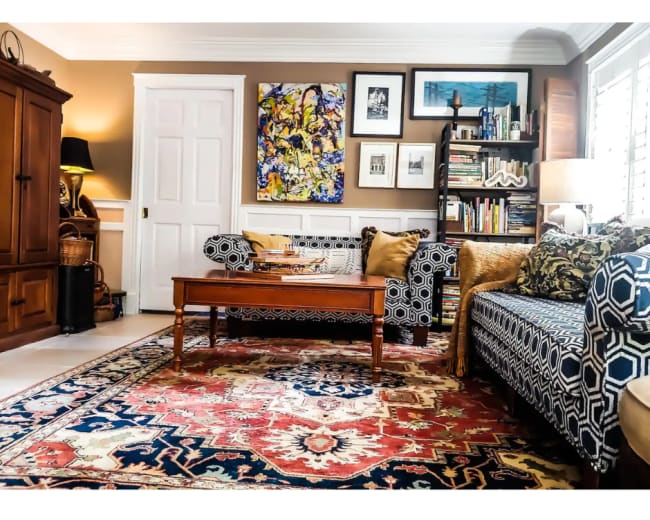 The living room features a patterned sofa, a wooden coffee table, and a bookshelf, all set against a backdrop of art on the walls and a large area rug.