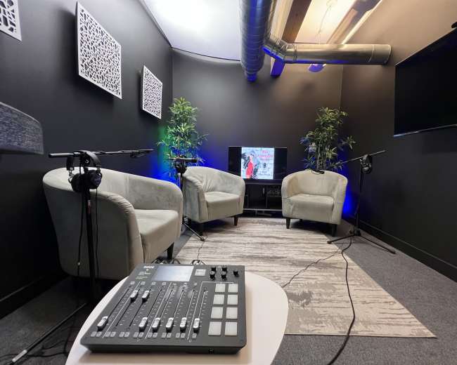 The image shows a small recording studio with two armchairs, a television, and audio equipment on a table.