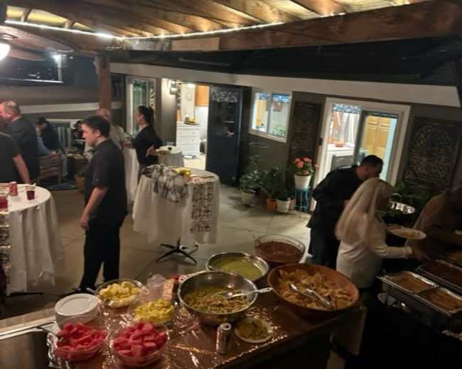 A gathering is taking place in an indoor-outdoor space with guests enjoying a buffet of food and drinks.
