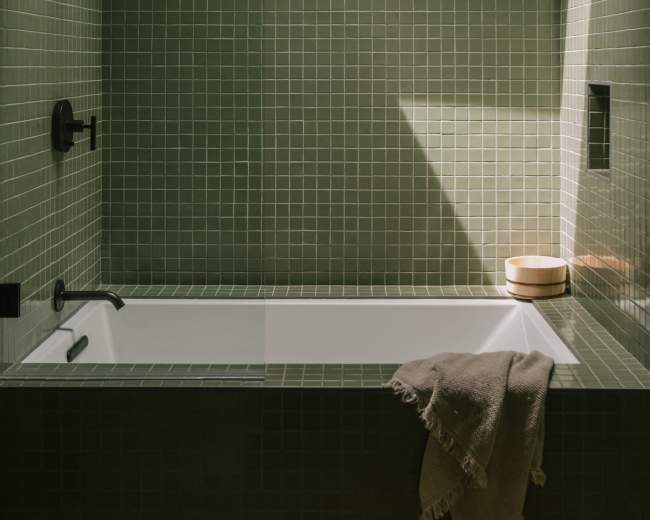 A bathroom features a green tiled wall, a bathtub, a skylight, and a towel draped over the edge of the tub.