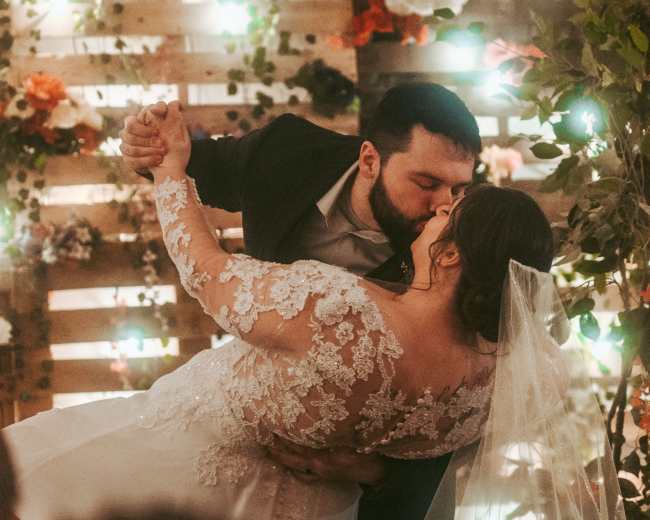 A couple shares a kiss as the groom lifts the bride in a decorated indoor wedding setting.