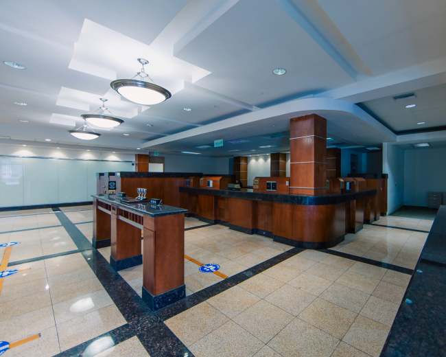 The image shows an empty office space with wooden reception counters, polished tile flooring, and overhead lighting.