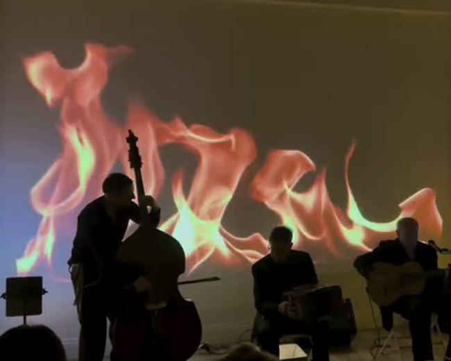 Musicians perform in front of a wall displaying a fiery projection.