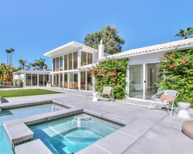 A modern house features a swimming pool and spa, surrounded by lush landscaping and bright blue skies.