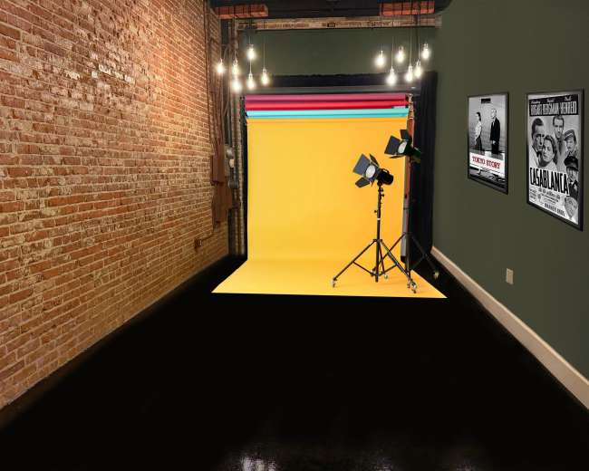 The image shows an interior studio space with a yellow backdrop, lighting equipment, exposed brick walls, and framed movie posters on the dark green side wall.