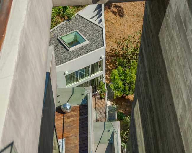 The image shows a modern architectural design featuring a multi-level structure with outdoor stairs, glass railings, and a view of green landscaping.