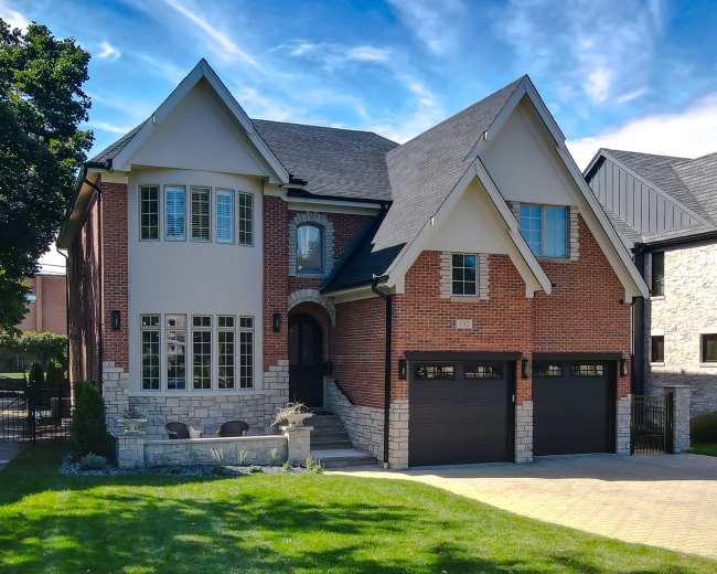 The image shows a modern two-story brick house with a stone foundation, featuring a driveway and well-maintained landscaping.