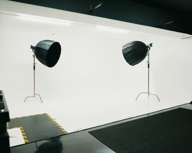 A photography studio with two large softbox lights positioned on stands, illuminating a seamless white backdrop.